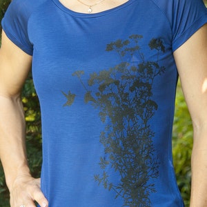 May include: A royal blue t-shirt featuring a black silhouette of a hummingbird and a cluster of flowers.