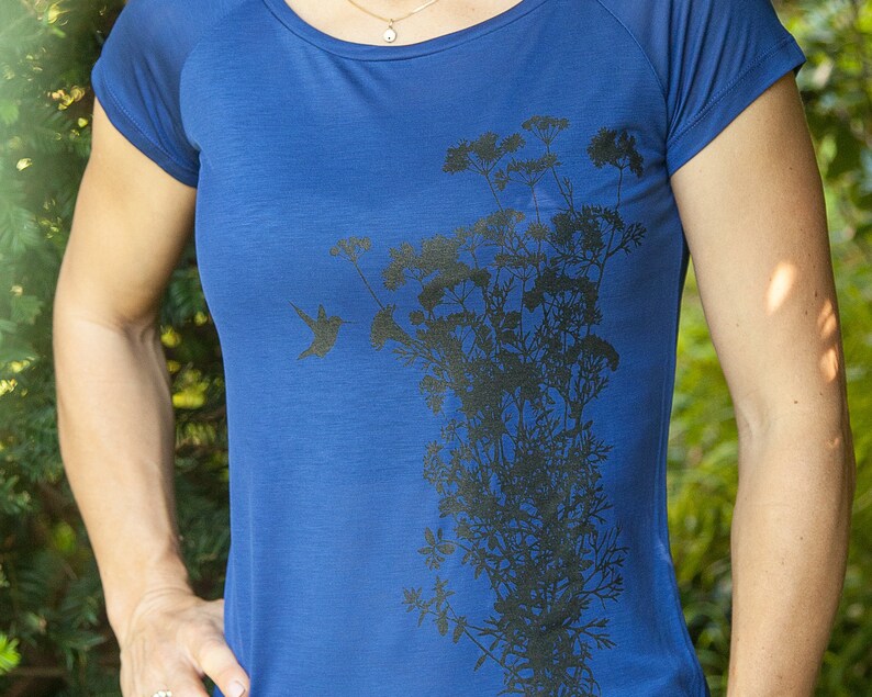 May include: A royal blue t-shirt featuring a black silhouette of a hummingbird and a cluster of flowers.
