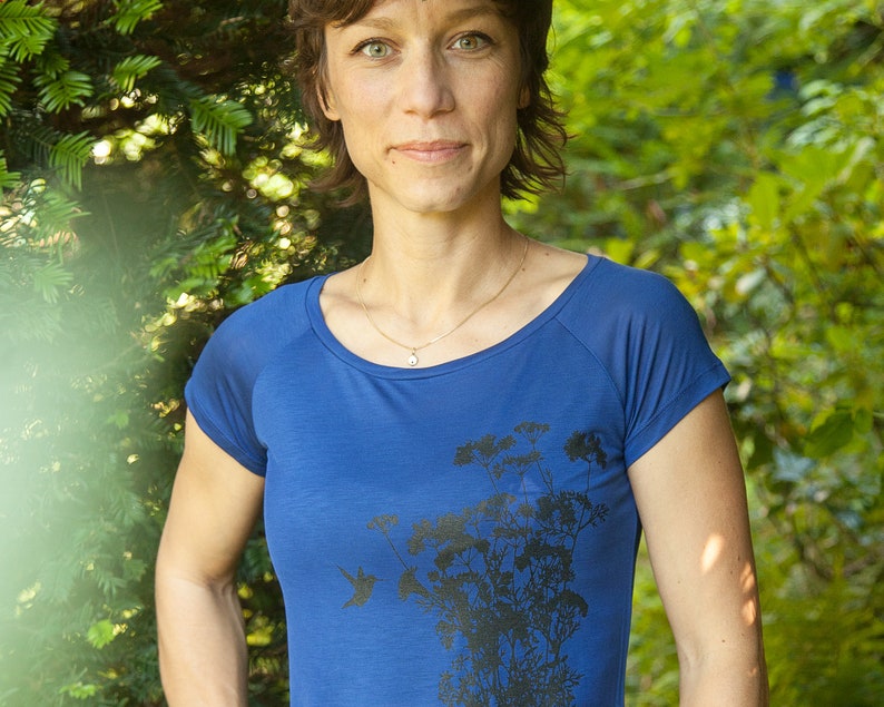 May include: A woman wearing a blue short-sleeved shirt with a black floral print. The shirt has a scoop neck and a relaxed fit.