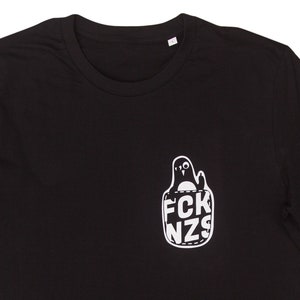 Może przedstawiać: Czarny T-shirt z białym nadrukiem pingwina w kieszeni z napisem "FCK NZS".