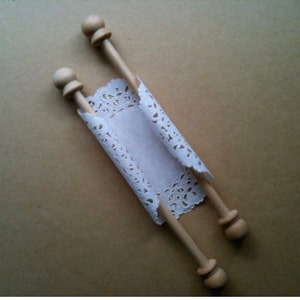 Puede incluir: Un rollo de encaje blanco con tacos de madera en cada extremo. El rollo está enrollado y atado con una cinta.