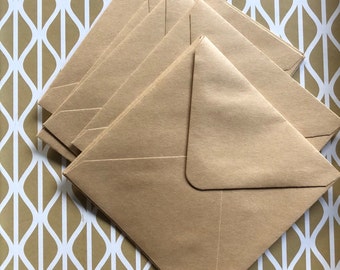 May include: A stack of six square, light brown envelopes arranged diagonally across a gold and white patterned surface. The envelopes are made of a textured paper and are closed.