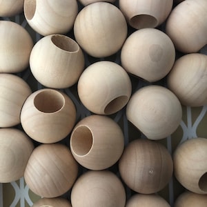 Może przedstawiać: Zbliżenie na grupę naturalnych drewnianych kulek z wyciętym otworem w każdej z nich. Kulki są ułożone w losowym wzorze i wszystkie są tej samej wielkości.