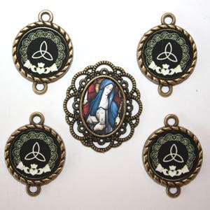 May include: Five antique bronze charms with Celtic knot designs and a single charm with a stained glass image of a woman in a blue robe. The charms have a black background with white accents.