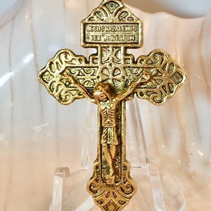 May include: A gold-toned metal crucifix with a detailed design. The inscription on the cross reads "JESUS NAZARENUS REX JUDAEORUM".