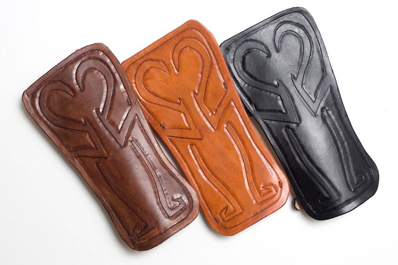 Puede incluir: Tres protectores de brazo de cuero con un dise&ntilde;o decorativo en relieve. Los protectores de brazo son marrones, tostados y negros.