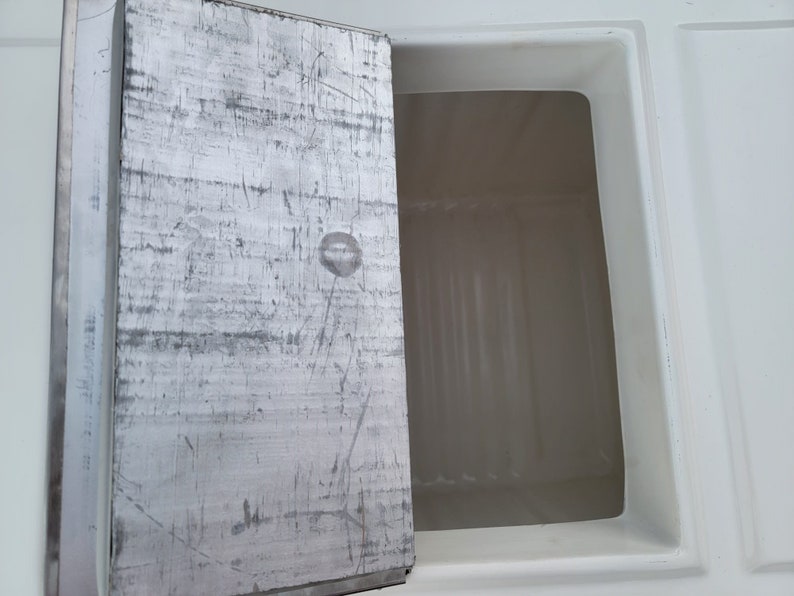 May include: A white rectangular compartment with a metal door that is open. The door has a silver finish and is scratched.