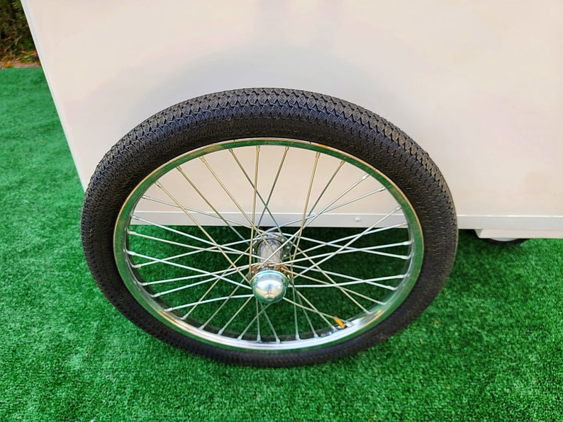 May include: A close-up of a black rubber tire with a silver spoke wheel. The tire is on a green artificial grass surface.