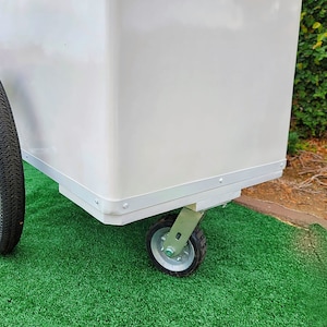 May include: White utility cart with a large rectangular body and four wheels. The cart has a silver trim around the edges of the body and the wheels are silver with black tires.