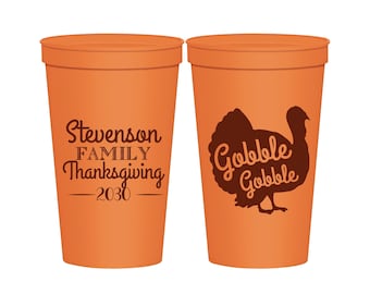 Könnte beinhalten: Zwei orangefarbene Stadionbecher. Auf einem Becher steht der Text "Stevenson FAMILY Thanksgiving - 2030". Der andere Becher hat eine braune Truthahn-Grafik mit den Worten "Gobble Gobble". Die Becher sind für Thanksgiving.
