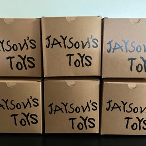 May include: Six brown cardboard boxes stacked in two rows of three. Each box has the words "Jayson's Toys" written in black marker.