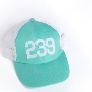 May include: A turquoise and white mesh baseball cap with the number "239" embroidered on the front.