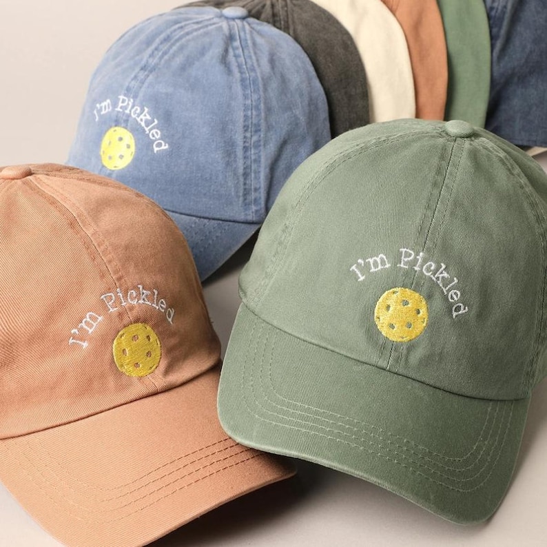 K&ouml;nnte beinhalten: Drei Baseballkappen in verschiedenen Farben, jede mit dem Schriftzug "I'm Pickled" und einem gestickten gelben Pickleball auf der Vorderseite.