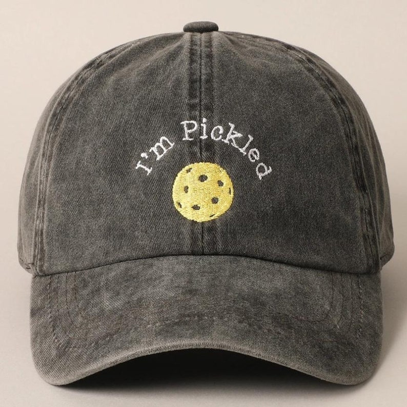 K&ouml;nnte beinhalten: Eine schwarze, abgenutzte Baseballkappe mit dem gestickten Text "I'm Pickled" in Wei&szlig; und einem gestickten gelben Pickleball in der Mitte.