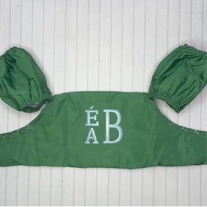 May include: Green fabric baby carrier with puffy sleeves and the embroidered initials "ÉA B".