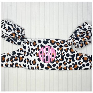 May include: A white and brown leopard print fabric baby carrier with a pink monogram "ARM" in the center.