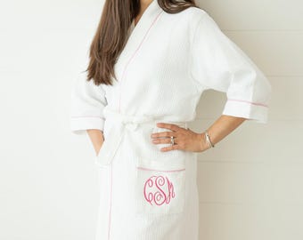 May include: A white waffle-weave robe featuring three-quarter length sleeves, a tie waist, and pink piping along the edges. A front pocket displays a pink embroidered monogram with the letters CSM in a decorative script font style.