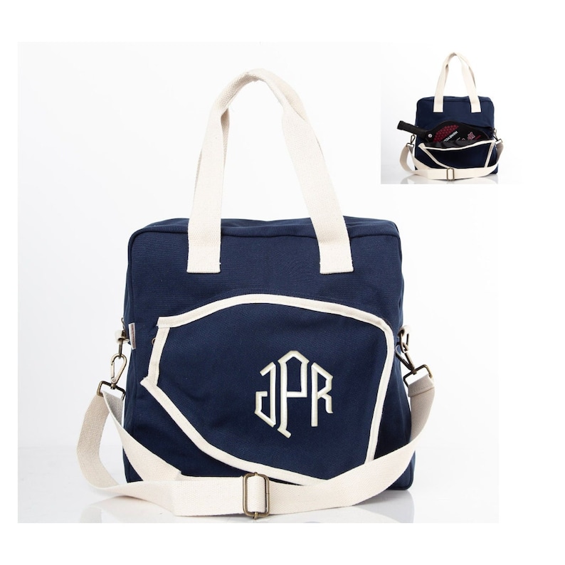 May include: A navy blue canvas tote bag with a white trim and a white monogram "JPR" on the front. The bag has a long adjustable strap and two top handles.