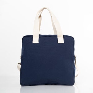 May include: A navy blue canvas tote bag with cream-colored handles. The bag has a zipper closure and a small pocket on the side.
