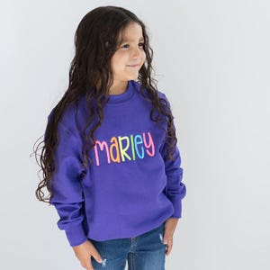 May include: A purple sweatshirt with the name "Marley" embroidered in rainbow colors.