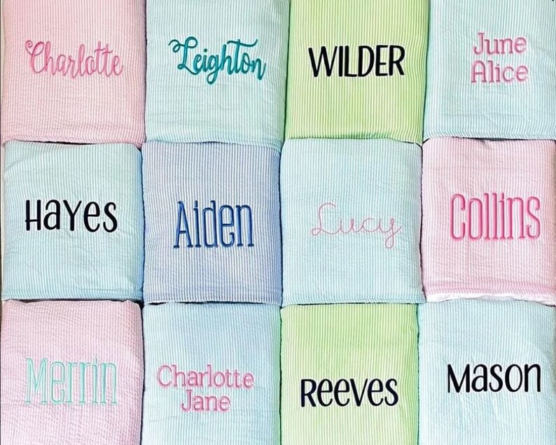 May include: Twelve personalized baby blankets in various colors, including pink, blue, and green. Each blanket features a different name embroidered in a contrasting color. The names include Charlotte, Leighton, Wilder, June Alice, Hayes, Aiden, Lucy, Collins, Merrin, Charlotte Jane, Reeves, and Mason.