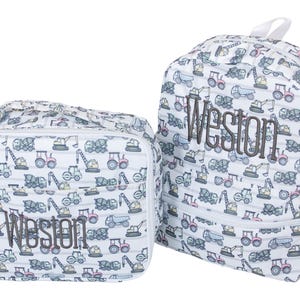 May include: A white lunch bag and a matching backpack, both featuring a repeating pattern of construction vehicles in blue, red, and yellow. Each item is personalized with the name Weston embroidered in dark gray thread on the front.