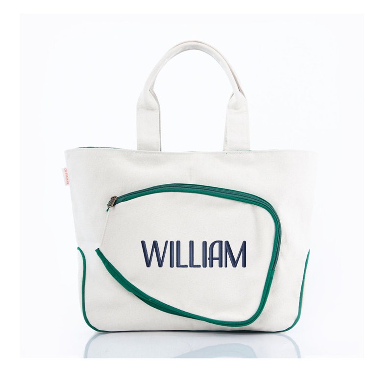 May include: White canvas tote bag with a green zippered pocket shaped like a tennis racket. The name "WILLIAM" is embroidered in navy blue on the pocket.