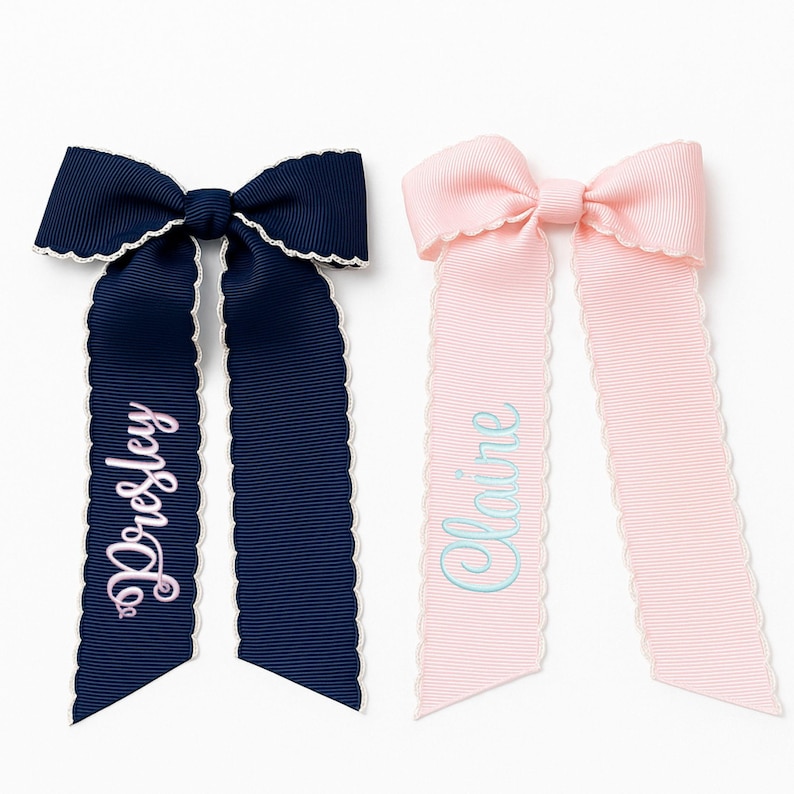 May include: Two grosgrain ribbon hair bows with scalloped white edges. The navy blue bow features the name Presley embroidered in light pink script, while the light pink bow features the name Claire embroidered in light blue script.