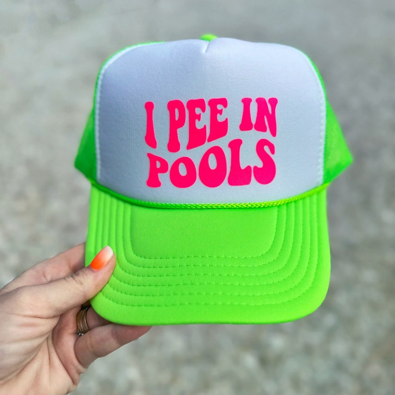 May include: A neon green and white trucker hat with the text "I PEE IN POOLS" in pink letters.