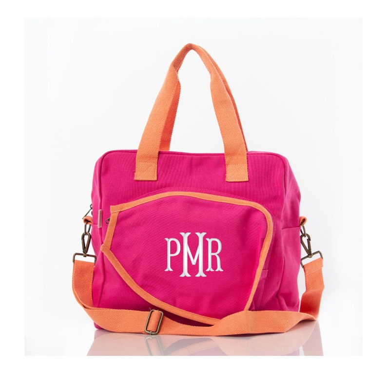May include: A pink canvas tote bag with orange handles and trim. The bag has a large pocket on the front with the monogram "PMR" embroidered in white.