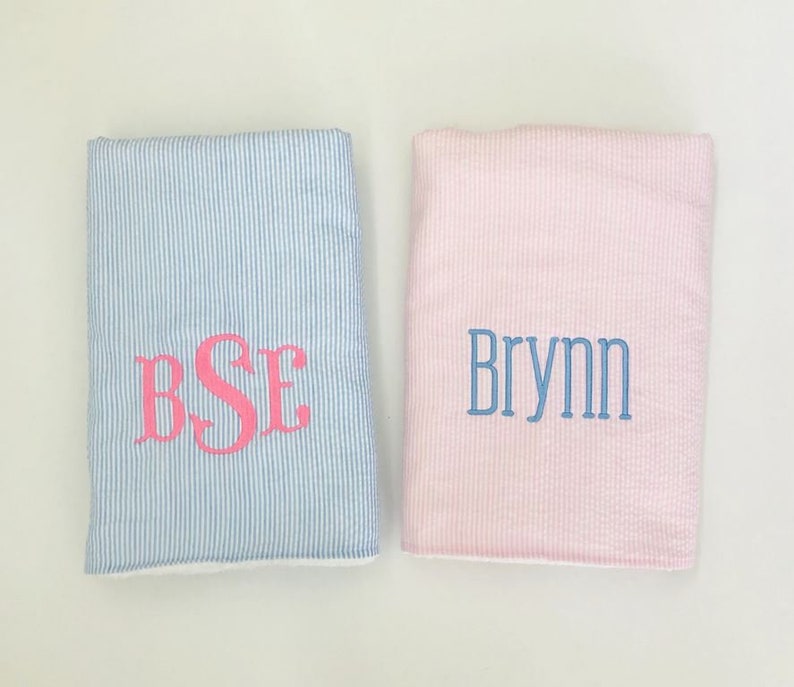 May include: Two baby blankets, one blue with white stripes and the monogram "BSE" in pink, and one pink with white stripes and the name "Brynn" in blue.