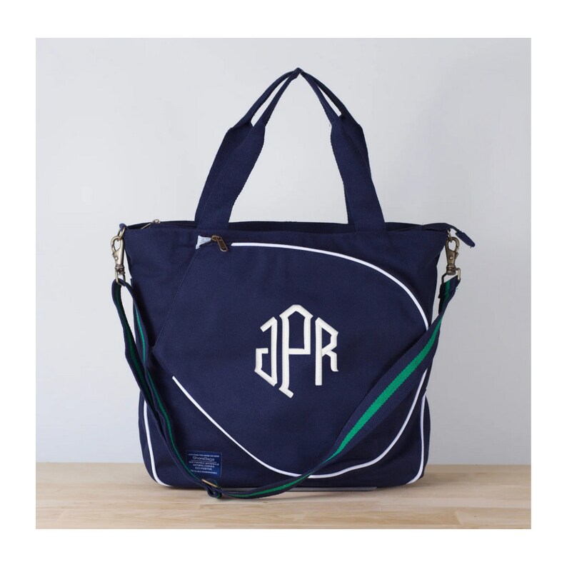 Puede incluir: Una bolsa de lona azul marino con un monograma blanco "JPR" y una correa de hombro verde y blanca.