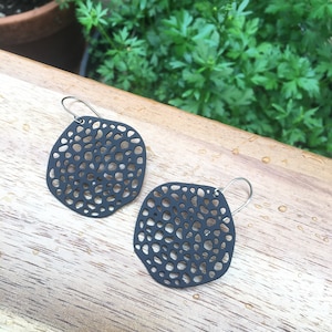 May include: A pair of black dangle earrings with a delicate, intricate, circular, openwork design. The earrings are made of a lightweight material and have a silver-toned hook.