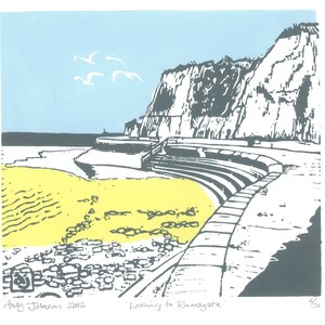 May include: A print of a coastal scene with a yellow beach, gray cliffs, and a blue sky. White seagulls fly above the cliffs. The print is titled "Looking to Ramsgate" and signed by Andy Johnson 2012.
