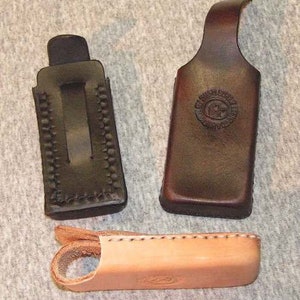 May include: Three leather holsters for small items. The holsters are brown and black with stitching detail. The holsters are made of leather and have a flap that closes with a snap.