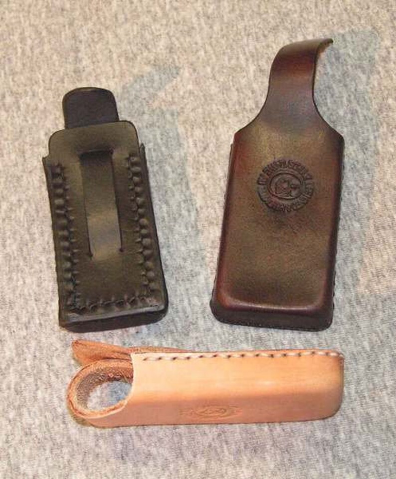 May include: Three leather holsters for small items. The holsters are brown and black with stitching detail. The holsters are made of leather and have a flap that closes with a snap.