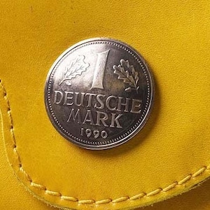 May include: A silver German 1 Deutsche Mark coin with the year 1990 inscribed on the bottom. The coin features two oak leaves and the words "Deutsche Mark" on the face.