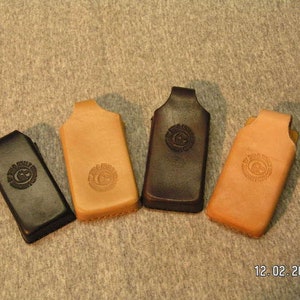 May include: Four leather phone cases, two are brown and two are black. Each case has a circular design embossed on the front.