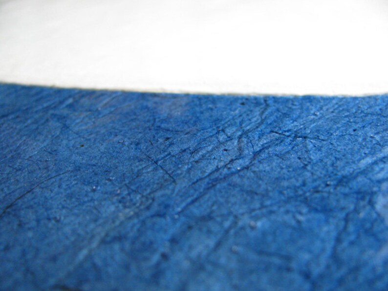 May include: Close-up of textured, deep blue paper with a white section at the top. The paper has a crinkled appearance with visible lines and subtle variations in color, creating a tactile and artistic effect. The image suggests a focus on texture and color.