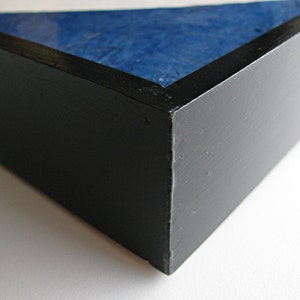 May include: Close-up of a black painted wooden frame with a blue and white textured surface visible inside. The frame has a matte finish and a clean, modern aesthetic. The corner of the frame is in focus.