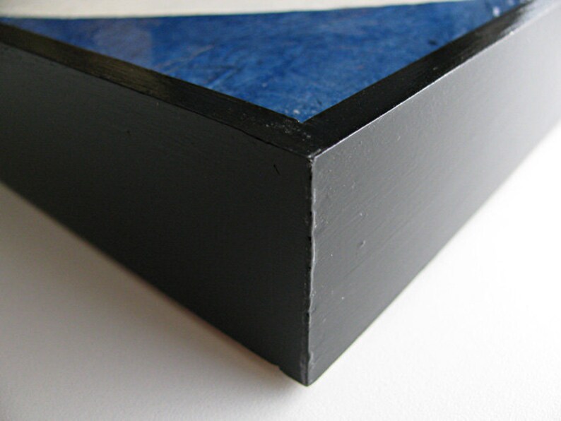May include: Close-up of a black painted wooden frame with a blue and white textured surface visible inside. The frame has a matte finish and a clean, modern aesthetic. The corner of the frame is in focus.