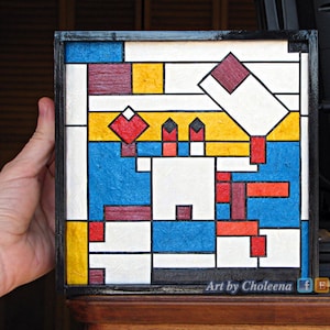 May include: A framed abstract geometric art piece with a black frame. The artwork features a variety of colors including red, yellow, blue, white, and brown. The artwork is titled "Art by Choleena".