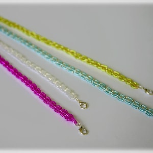 May include: Four beaded bracelets in different colours: pink, white, light blue, and yellow. The bracelets are made of small, round beads and have a simple, elegant design.