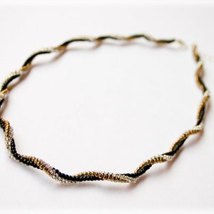 Pode incluir: Um colar delicado e trançado feito de contas pretas, prateadas e douradas. O colar é um design simples e elegante que seria perfeito para o uso diário.