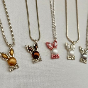 May include: Five silver chain necklaces with beaded bunny pendants. The bunnies are in different colors: gold, brown, pink, white, and gray.