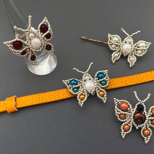 以下が含まれることがあります： リング、ヘアクリップ、ブレスレット、ブローチを含む、ビーズでできた蝶のジュエリー4点セット。蝶は銀色のビーズで作られており、カラフルなアクセントが施されています。
