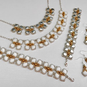 Op de afbeelding: Een set zilveren en gouden kralen sieraden met een bloemenontwerp. De set bevat een ketting, armband en oorbellen.