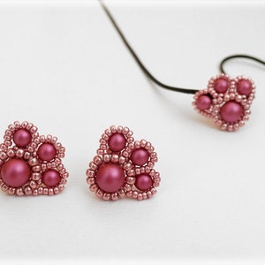 Op de afbeelding: Een set roze parel oorringen en een bijpassende ketting. De oorringen en ketting zijn gevormd als een poot afdruk met vijf roze parels in het midden.