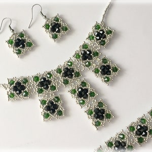 May include: A beaded jewelry set featuring a necklace, bracelet, and earrings. The set has a silver-tone base with black and green accents. The earrings are a square shape with a hook closure. The necklace and bracelet have a similar design.