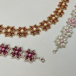 Puede incluir: Dos collares de cuentas con abalorios en forma de flor. Un collar está hecho con cuentas doradas y rosadas, el otro con cuentas plateadas y rosadas.